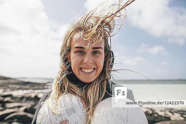 France  Brittany  Landeda  portrait of smiling young woman holding parts of a globe at the coast
