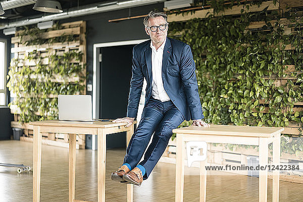 Mature businessman leaning on tables in green office