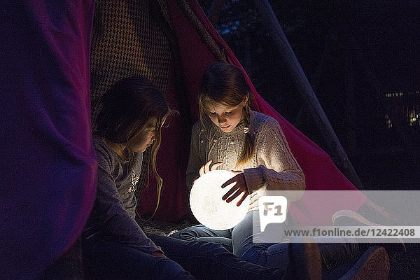 Two girls sitting in tipi  holding lamp as moon