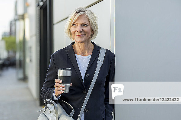 Smiling senior businesswoman with takeaway coffee outdoors