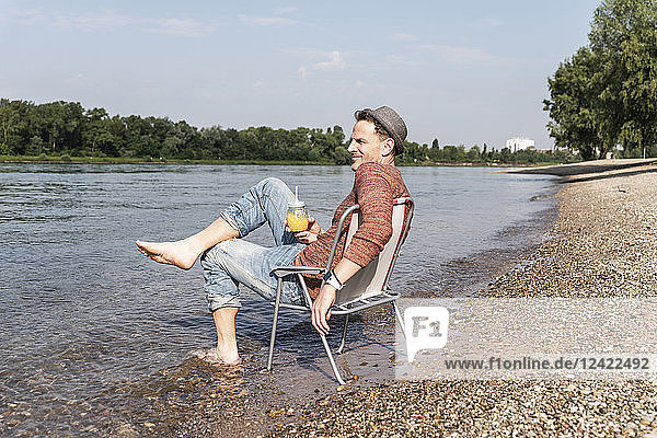 Mature man sitting on chair at Rhine riverbank