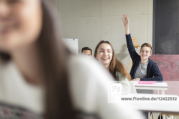 Smiling teenage boy raising hand in class