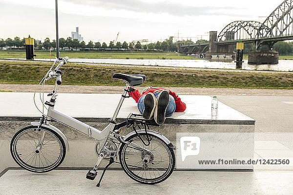 Senior woman with city bike having a break lying on platform