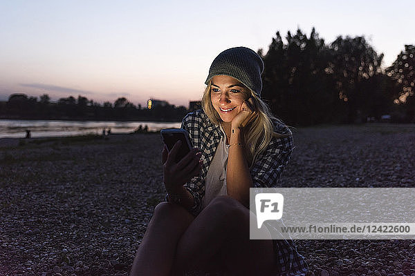 Young woman using smartphone on riverside in the evening