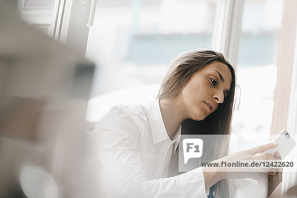 Young businesswoman sitting at window  using smartphone