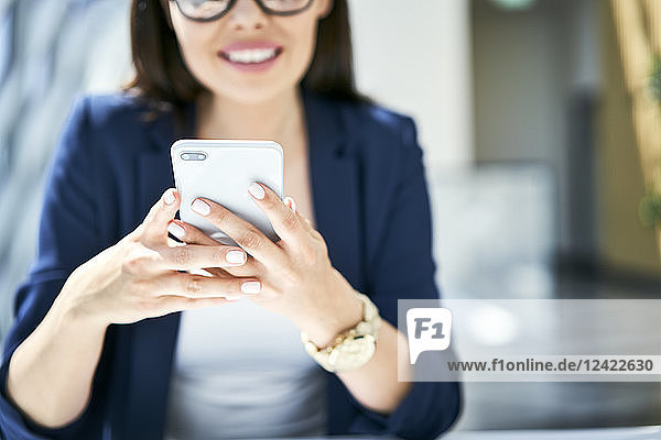 Close-up of smiling businesswoman using cell phone in office