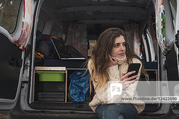 Portrait of young woman with cell phone sitting in van