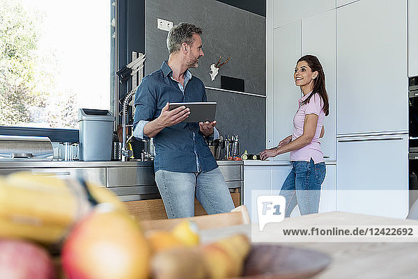 Couple in kitchen at home cooking and using a tablet