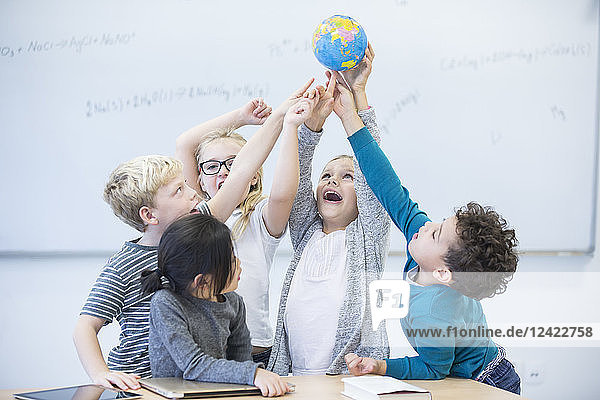 Happy pupils holding globe together in class