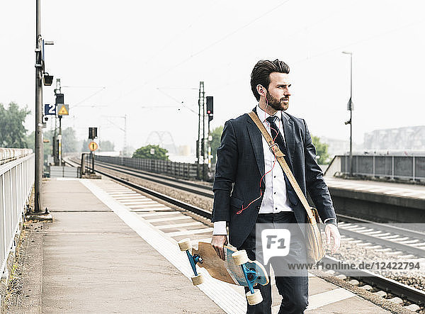 Businessman with skateboard and earphones walking at the platform
