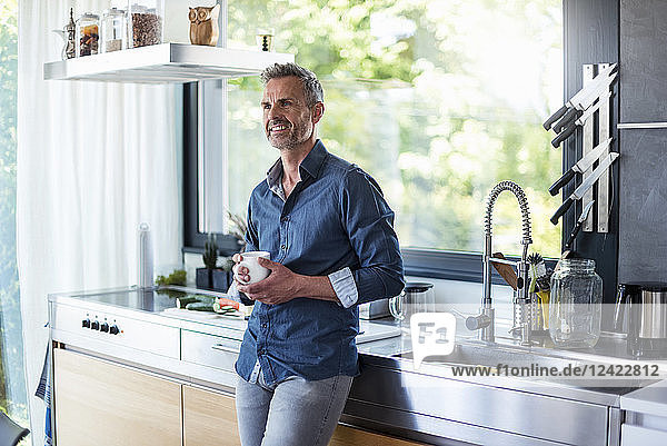 Smiling mature man at home in kitchen with cup of coffee