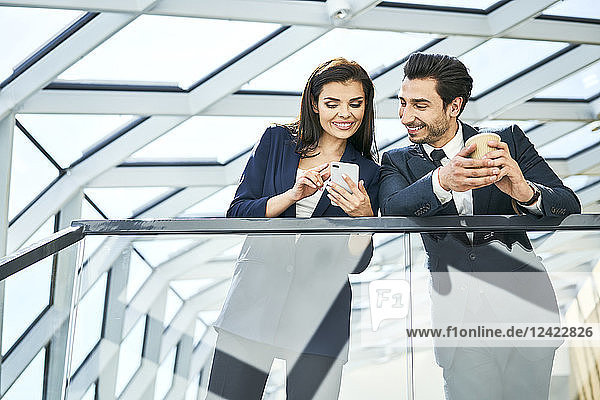Smiling businesswoman and businessman sharing cell phone in modern office