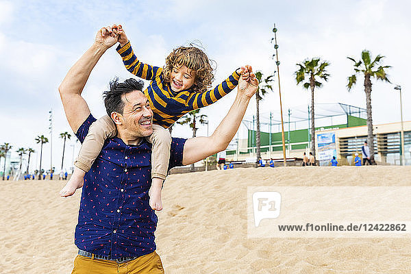 Spain  Barcelona  father with son on the beach giving a piggyback ride