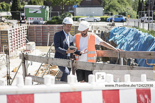Man in suit with tablet talking to construction worker on construction site