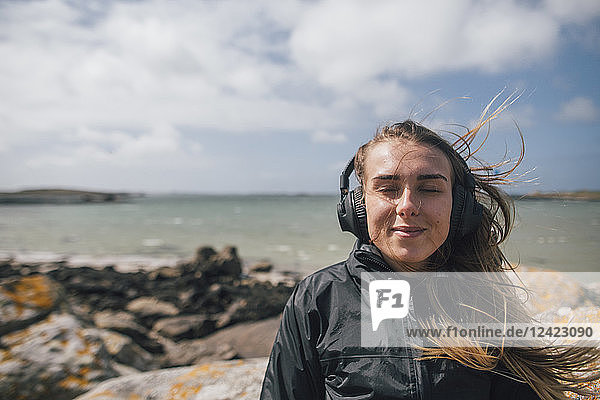 France  Brittany  Landeda  smiling young woman wearing headphones at the coast