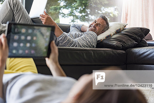 Couple relaxing in living room at home using tablet and laptop