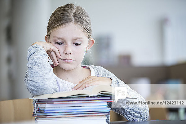 Schoolgirl reading book on table in school