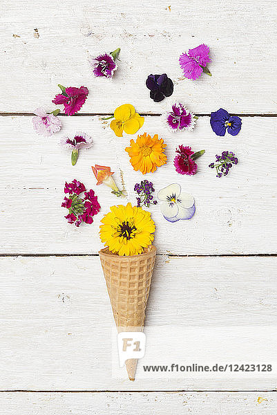 Ice cream cone and edible flowers on white wood