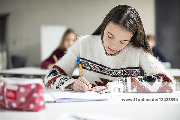 Teenage girl writing in exercise book in class