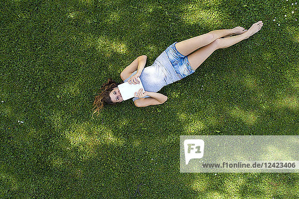 Young woman lying on meadow  using tablet