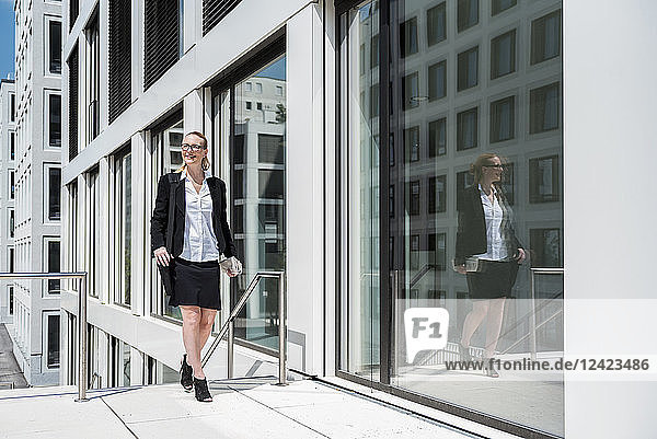 Smiling businesswoman with newspaper walking in front of office building