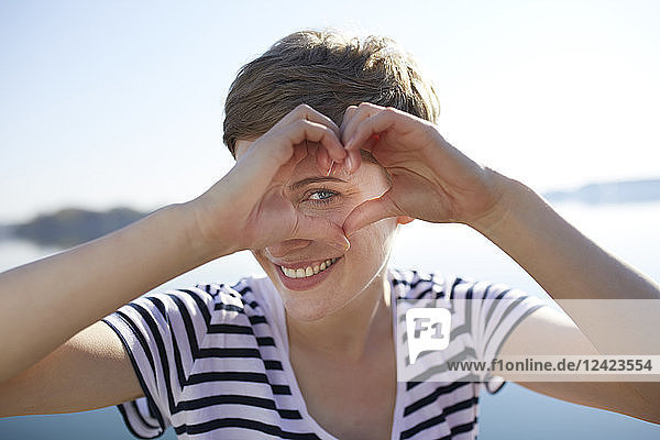 Portrait of smiling woman in front of lake shaping heart with her fingers