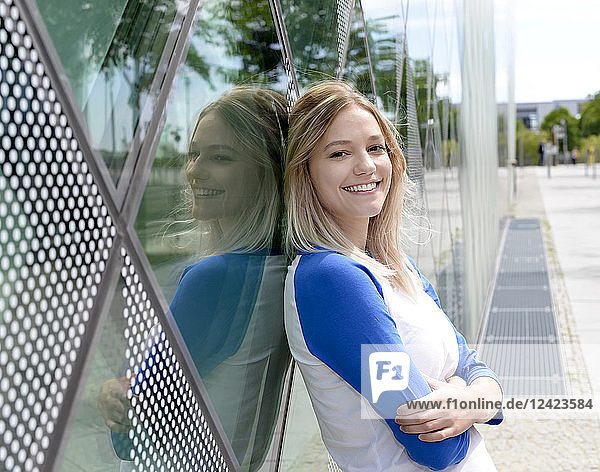 Smiling blond young woman leaning on a glass facade