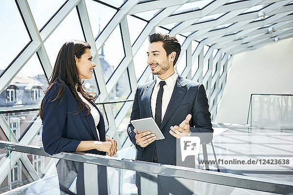 Businesswoman and businessman with tablet talking in modern office