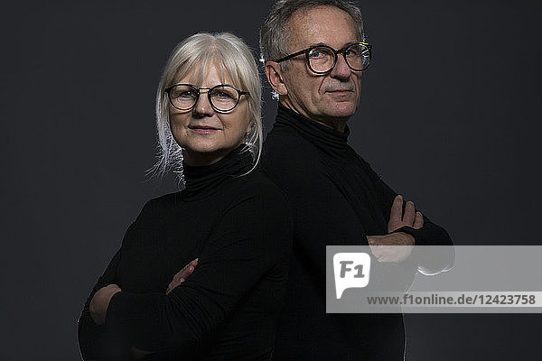Portrait of senior couple wearing glasses in front of dark background