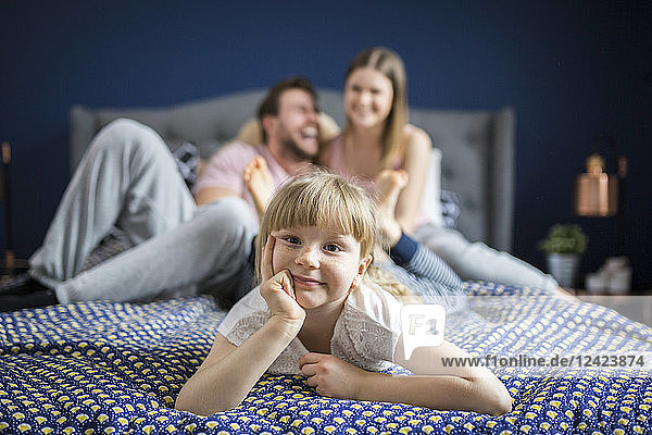 Cheeky little girl lying on bed with her parents