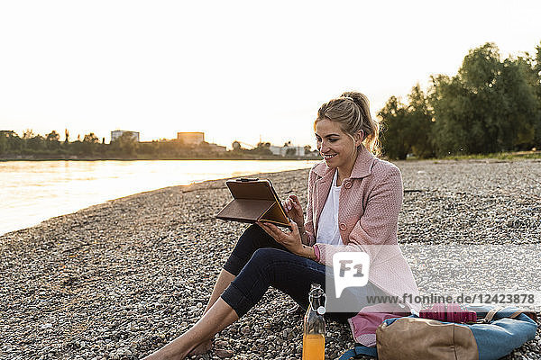 Young blond woman using tablet on riverside in the evening