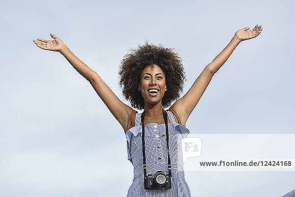 Portrait of happy young woman with camera against sky