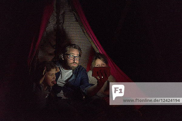 Father and daughters sitting in tent  taking a selfie