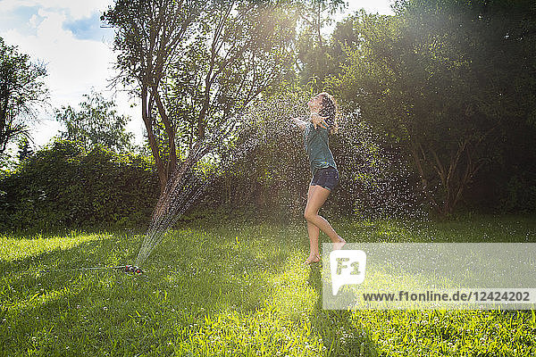 Girl having fun with lawn sprinkler in the garden