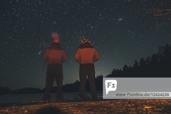 Sweden  Sodermanland  two men standing at lakeside under starry sky at night