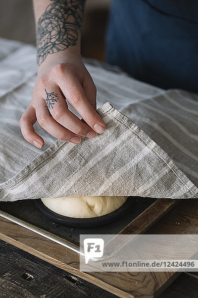 Woman covering vegan burger rolls on baking tray