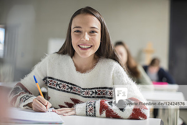 Portrait of smiling teenage girl writing in exercise book in class