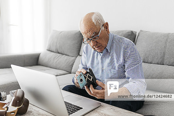 Senior man using laptop and holding his old photo camera
