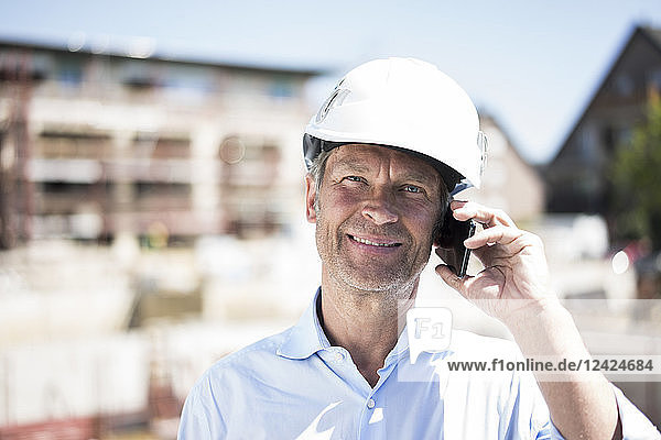 Portrait of smiling man wearing hard hat on cell phone on construction site