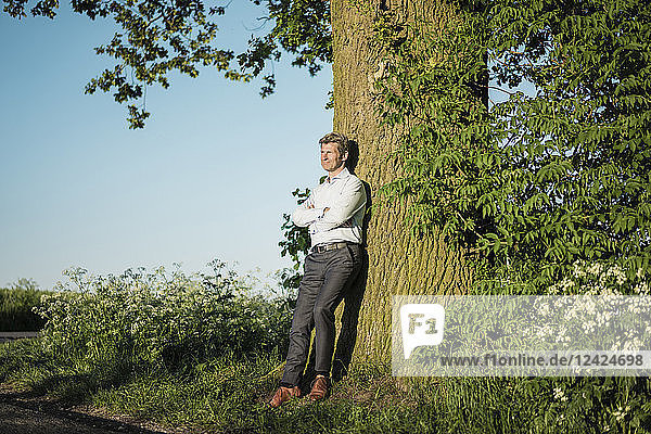 Businessman leaning on tree