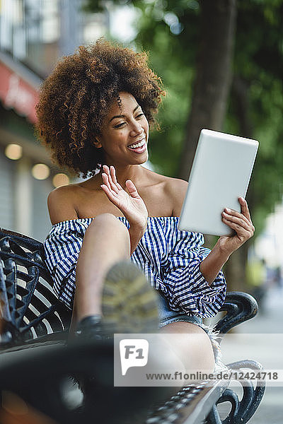 Smiling young woman sitting on bench with tablet having video chat