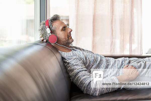 Relaxed mature man lying on couch at home wearing headphones