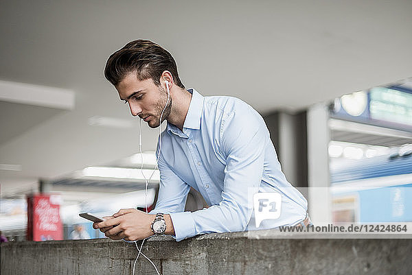 Businessman with cell phone and earbuds at the station