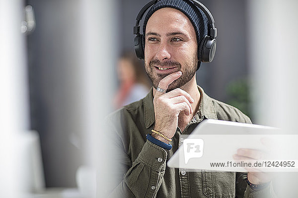 Portrait of smiling young man with headphones and tablet in office