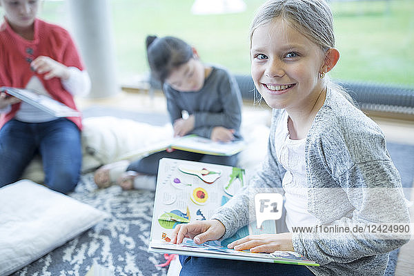 Portrait of smiling schoolgirl sitting on the floor with book in school break room