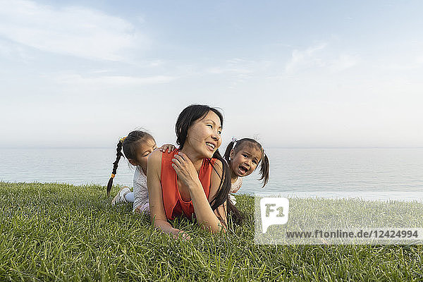 Mother with two daughters lying in grass at the coast