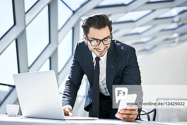 Smiling businessman looking at cell phone at desk in modern office