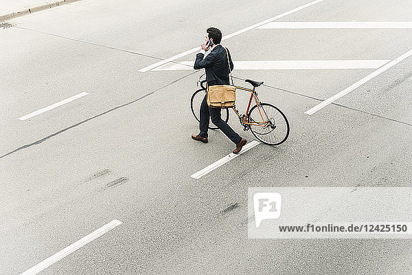 Businessman with bicycle on cell phone walking on the street