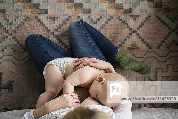 Mutter stillt ein Mädchen (12-17 Monate) auf einem Teppich sitzend