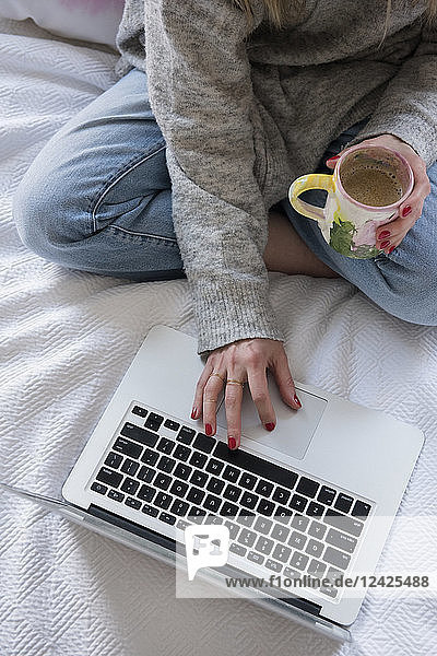 Frau mit Kaffee und Laptop im Bett